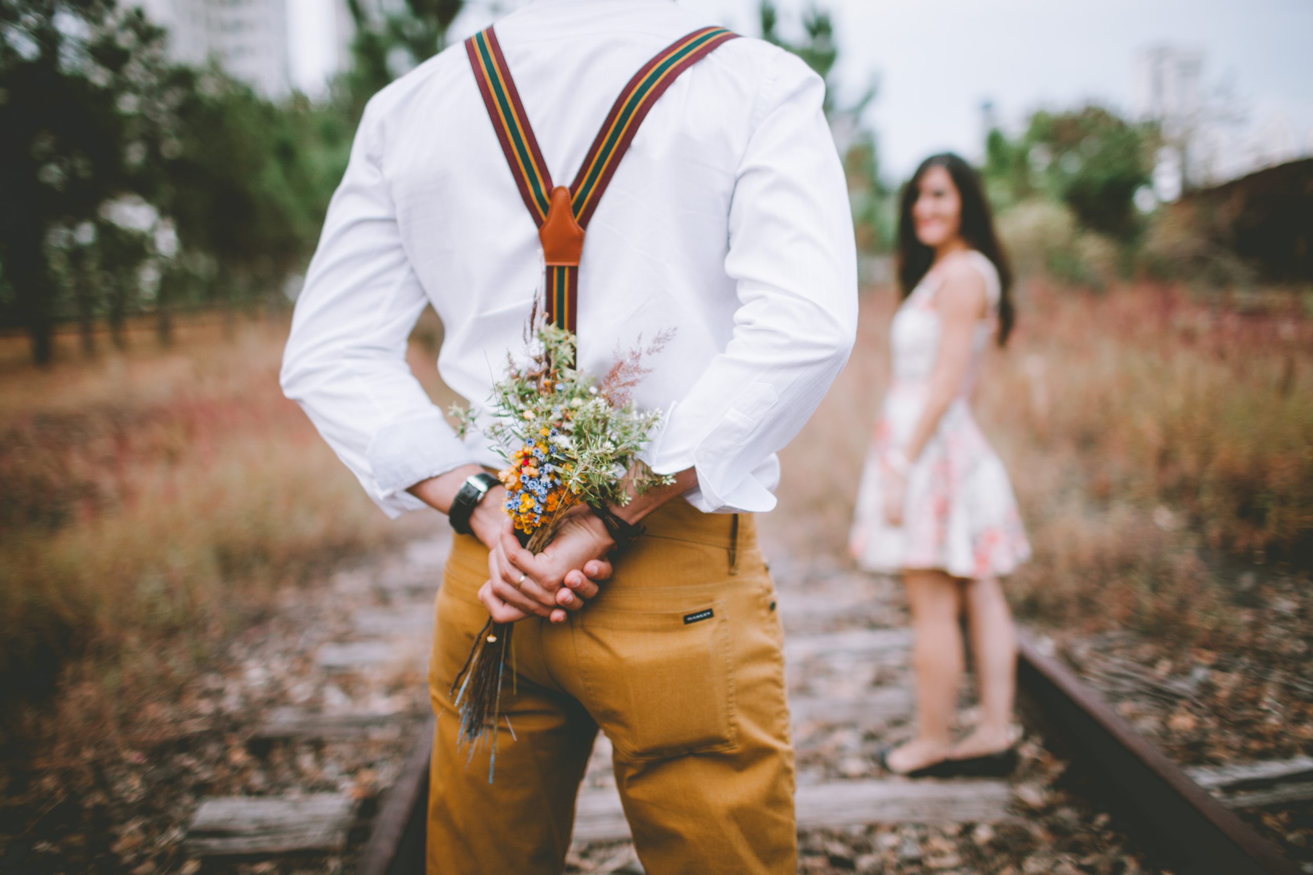 Man with bouquet in hands behind his back in front of woman